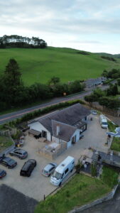 Drone photo of an L shaped house surrounded by green countryside